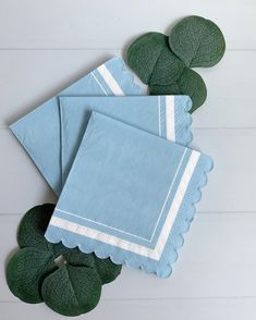 three blue napkins with white scalloped edges and green leaves on the side