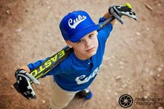 a young boy holding a baseball bat on top of a dirt field with his hands in the air