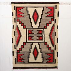 an old navajo rug hanging on the wall in a room with white walls and red accents