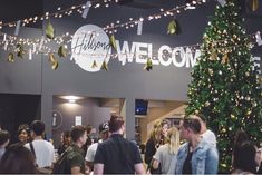 a group of people standing in front of a christmas tree with lights on the ceiling