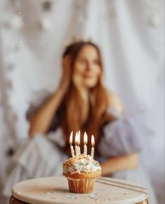 a cupcake with lit candles sitting on top of a table next to a woman