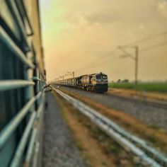 a train traveling down tracks next to a grass covered field with power lines in the background