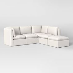 a white sectional couch with pillows on the top and bottom, sitting in front of a gray background