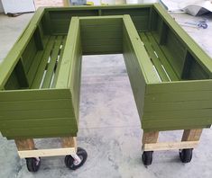 two green planters sitting on top of wooden pallets in a garage with wheels