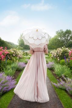 a woman in a pink dress holding an umbrella over her head while walking down a path