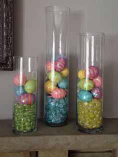 three glass vases filled with colorful balls on top of a table next to a mirror