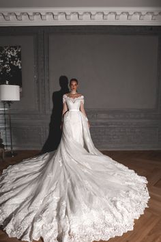 a woman in a white wedding dress standing on a wooden floor with her arms behind her back