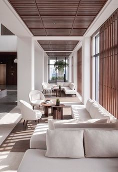 a living room filled with white couches and wooden ceilinging next to tall windows