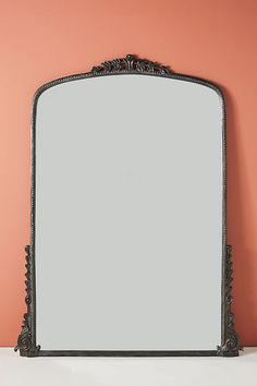 a mirror sitting on top of a white counter next to a pink wall and vase