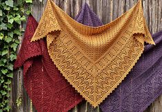 three knitted shawls hanging on a wooden fence with ivy growing around them,