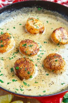 four scallops in a creamy sauce with lemon wedges