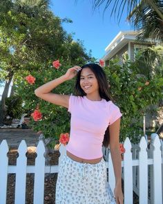 a woman standing in front of a white picket fence with her hand on her head