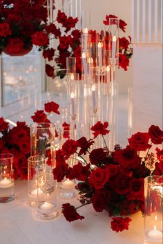 red flowers and candles are arranged on a white table with glass vases in the center