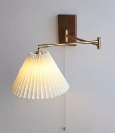 a wall light with a white pleated shade hanging from it's side on the wall