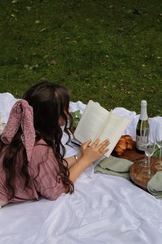 a woman sitting on the ground reading a book and holding a wine glass in her hand