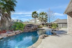 an outdoor swimming pool surrounded by rocks and palm trees in front of a brick house