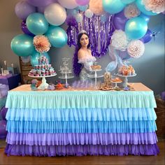 a table topped with cake and balloons next to a woman in a white dress sitting at a table