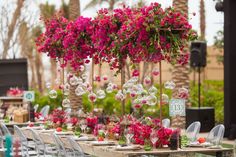 a long table with chairs and flowers hanging from it's ceiling in front of palm trees