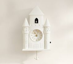 a white clock mounted to the side of a wall with a castle design on it