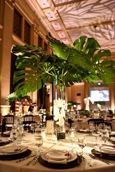 a tall vase filled with green leaves on top of a table