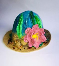 a blue and green hat with pink flowers on the front, sitting on top of sand