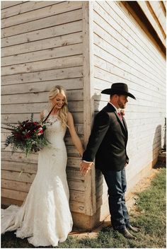 a bride and groom hold hands as they lean against a wooden wall holding bouquets