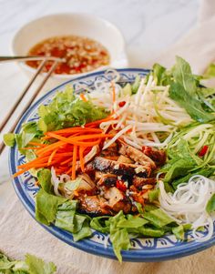 a blue and white plate topped with salad next to a bowl filled with meat, veggies and sauce