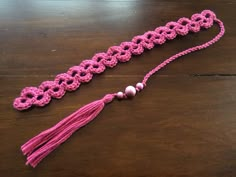 a pink crocheted tassel with beads and pearls on a wooden table top