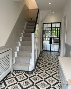 a hallway with stairs and tiled flooring next to a white door leading to a foyer