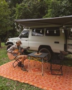 a man sitting in a chair under a tent next to a white truck playing the guitar