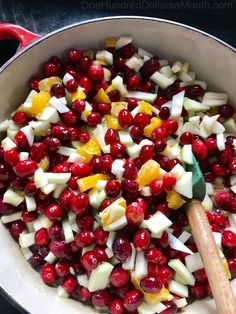 cranberries and apples are mixed together in a large pot with a wooden spoon