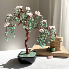 a bonsai tree with white flowers and green leaves on a table next to a wicker basket