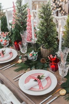 the table is set for christmas dinner with candles and greenery on it, along with other holiday decorations