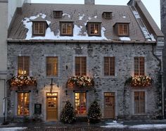 an old stone building with christmas lights on the windows and wreaths hanging from it