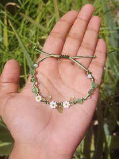 a hand holding a bracelet with flowers and leaves on it's string, in front of some grass