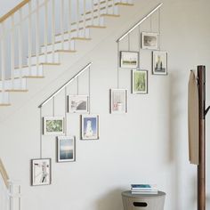 a white staircase with pictures on the wall and a trash can under it next to a stair case