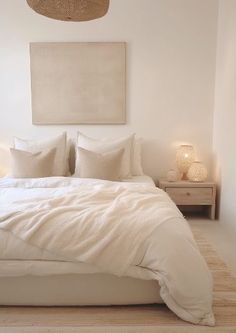 a bed with white linens and pillows in a small room next to a painting on the wall