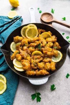 a skillet filled with chicken and lemons on top of a blue towel next to some chopsticks