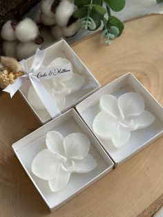 three boxes with white flowers in them sitting on a wooden table next to cotton balls