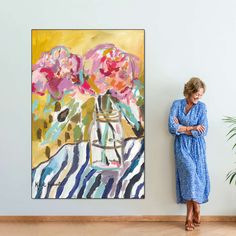 a woman standing in front of a painting next to a plant and potted plant