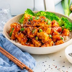 a bowl filled with chicken and broccoli next to chopsticks on a table