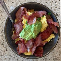 a black bowl filled with bacon, eggs and guacamole on top of a table