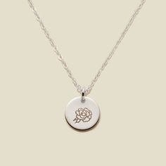 a necklace with a rose engraved on the front and back, hanging from a silver chain