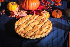 a pie sitting on top of a blue table cloth next to pumpkins and leaves