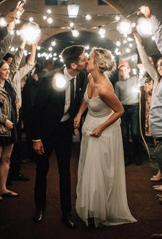 a newly married couple kissing in front of their guests with sparklers on the ground