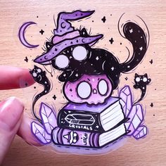 a hand holding a sticker with an image of a cat wearing a witches hat