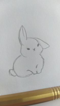 a pencil drawing of a rabbit sitting on top of a piece of paper next to a pen