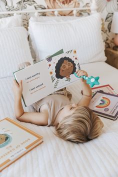 a little boy laying on top of a bed holding a book and reading it to someone