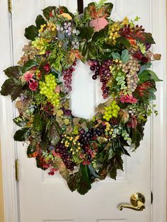 a wreath hanging on the front door of a house with grapes, leaves and other flowers