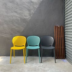 three different colored chairs sitting in front of a gray wall next to a radiator